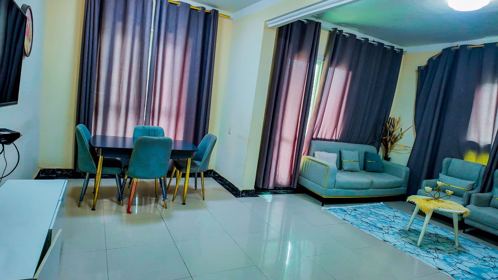 Open-plan living room with a dining table and grey sofas beside tall curtained windows