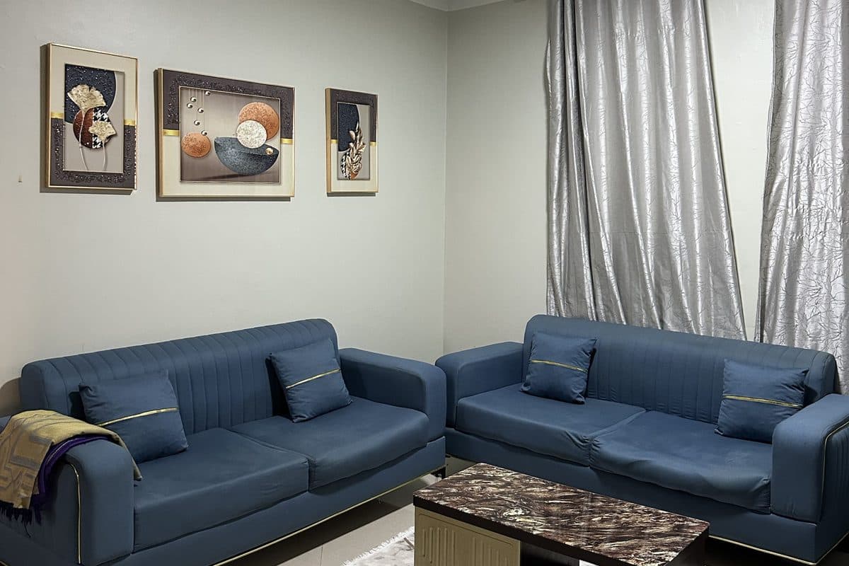Living room with two blue velvet sofas trimmed in gold, a marble-effect coffee table, three framed artworks and silver-grey curtains