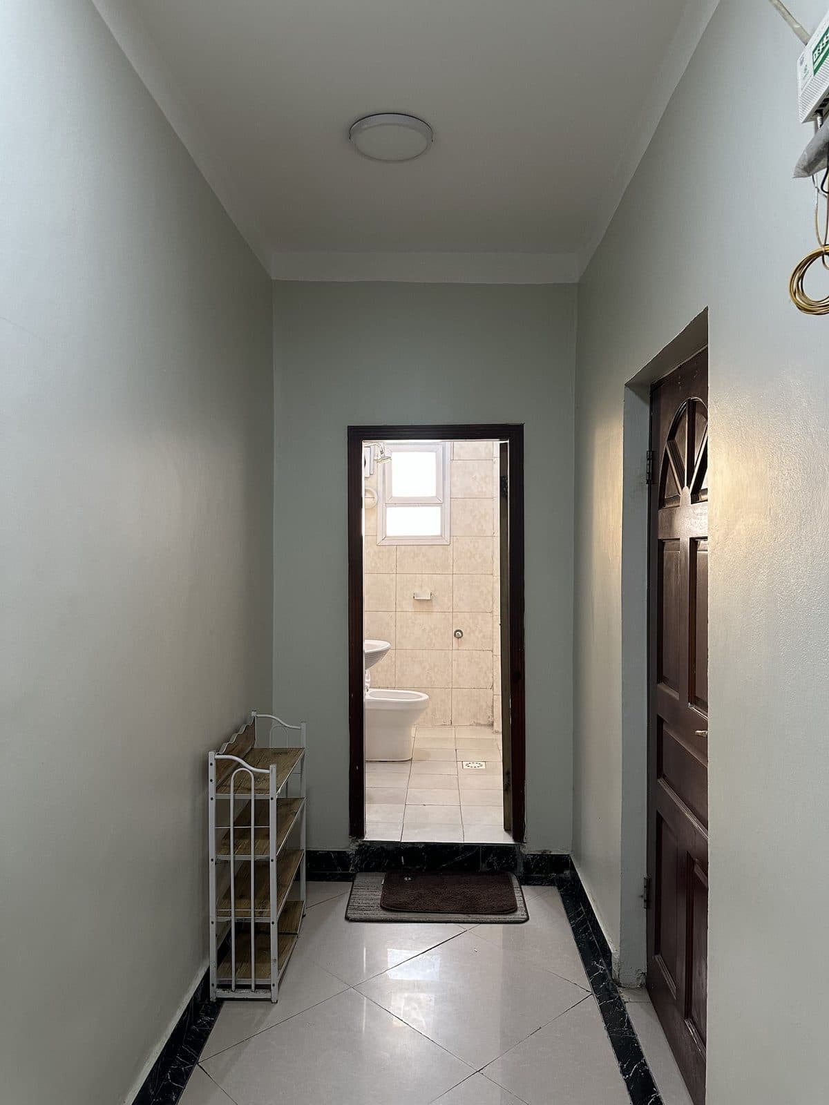 Hallway with a small shoe rack, looking through an open doorway into a white-tiled bathroom