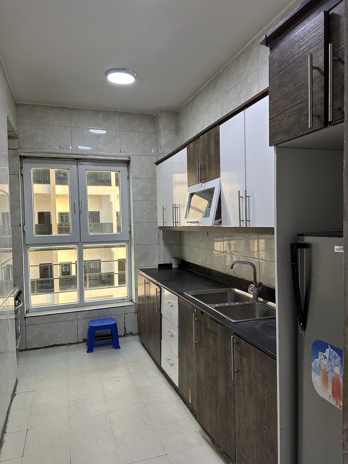 Galley kitchen with white and dark-wood cabinets, a black worktop with a double stainless-steel sink and a tall window