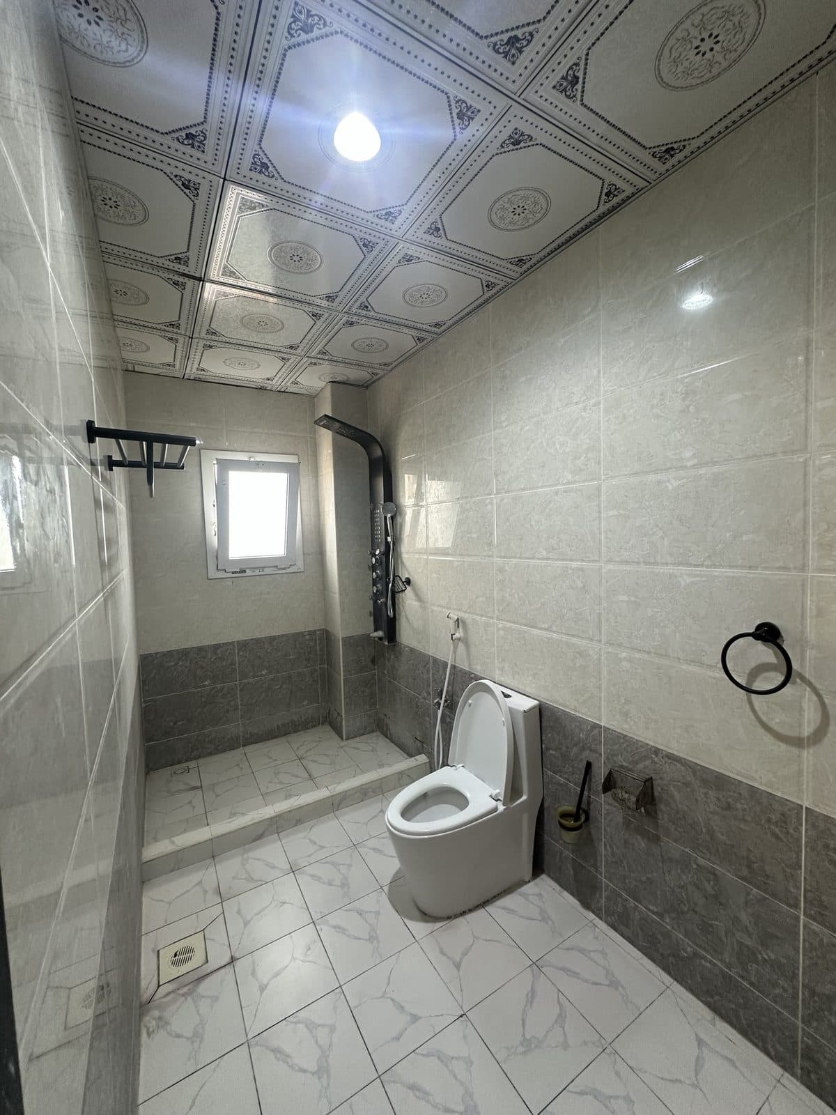 Tiled bathroom with a walk-in shower, a black shower column, a toilet and a small window
