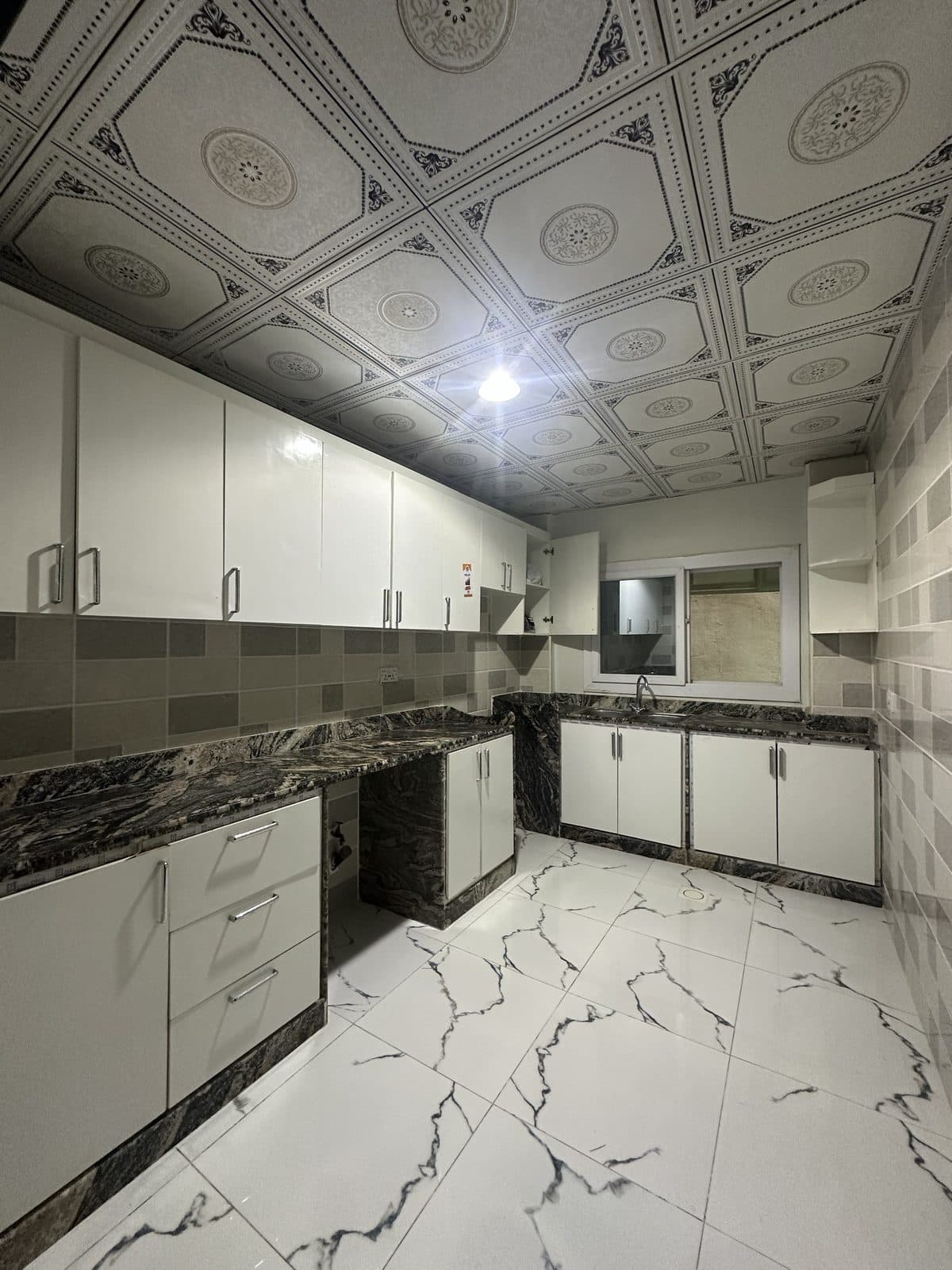 Kitchen with white gloss cabinets, dark marble worktops, a mosaic tile splashback and a sink beneath a small window